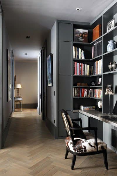 Dark hallway study with bookshelves, a cowhide-patterned chair, and a desk against one wall