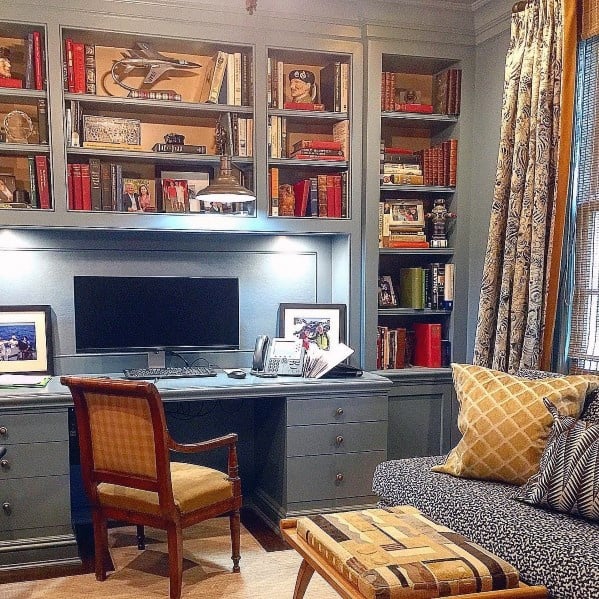 Traditional home office with built-in bookcases and a central desk, featuring elegant gray cabinetry, warm lighting, and personalized decor for a sophisticated yet cozy workspace