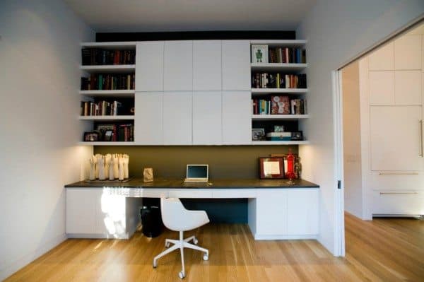 Modern home office with built-in shelves, a sleek built-in desk, and laptop, featuring wooden floor and white chair