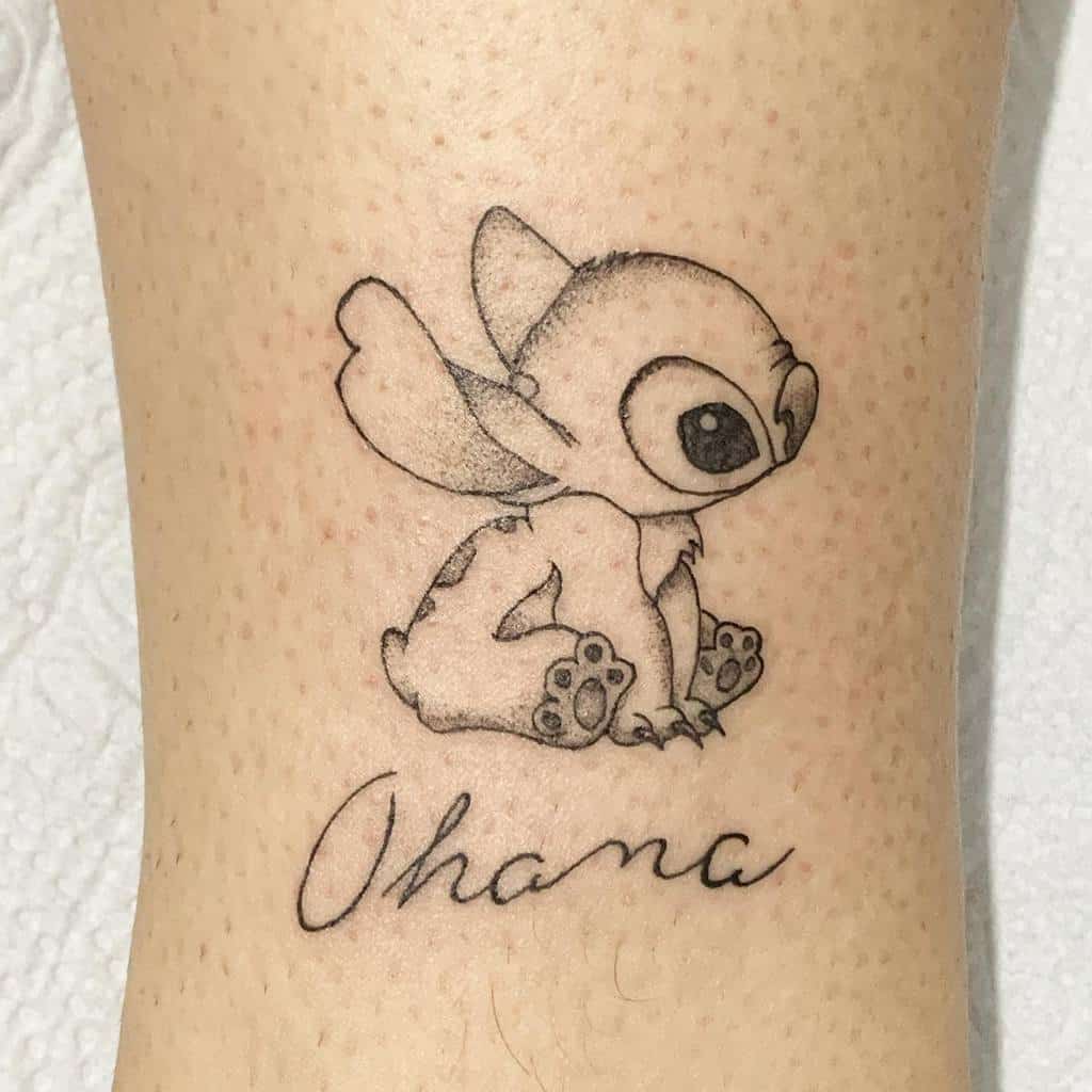 Black and white tattoo of Stitch from Lilo & Stitch sitting with the word 'Ohana' written below, on the calf.