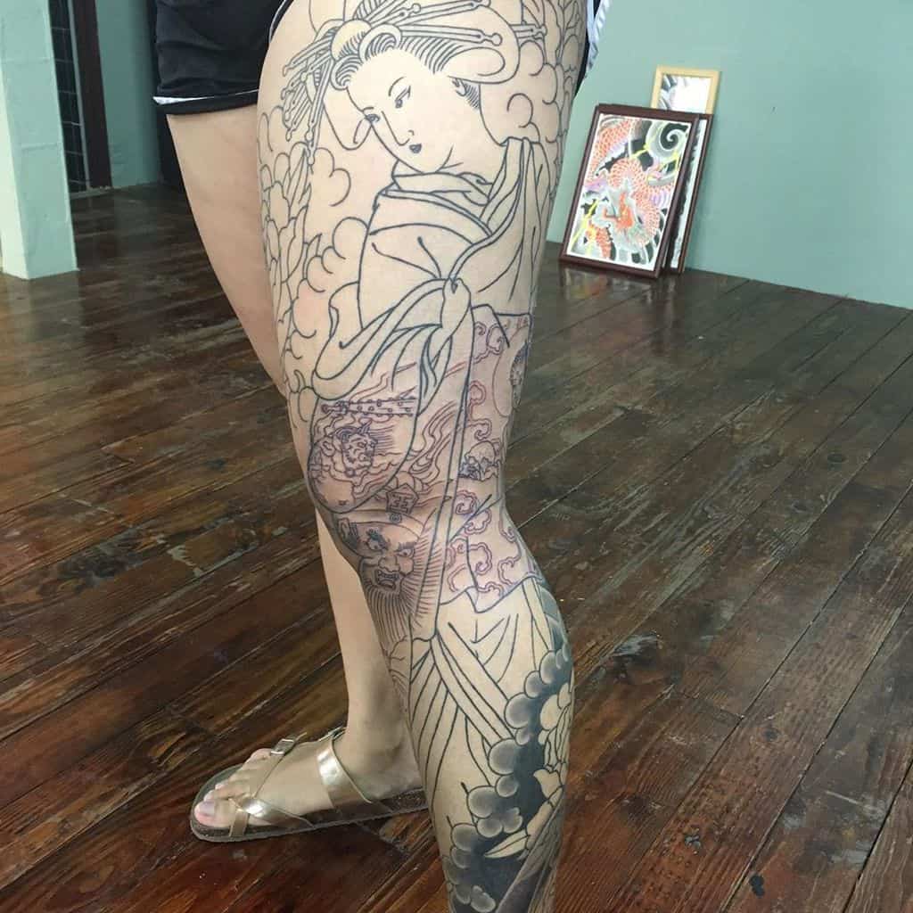 Large Japanese-style leg tattoo in progress, featuring a Geisha in flowing robes with intricate floral patterns and swirling cloud designs.