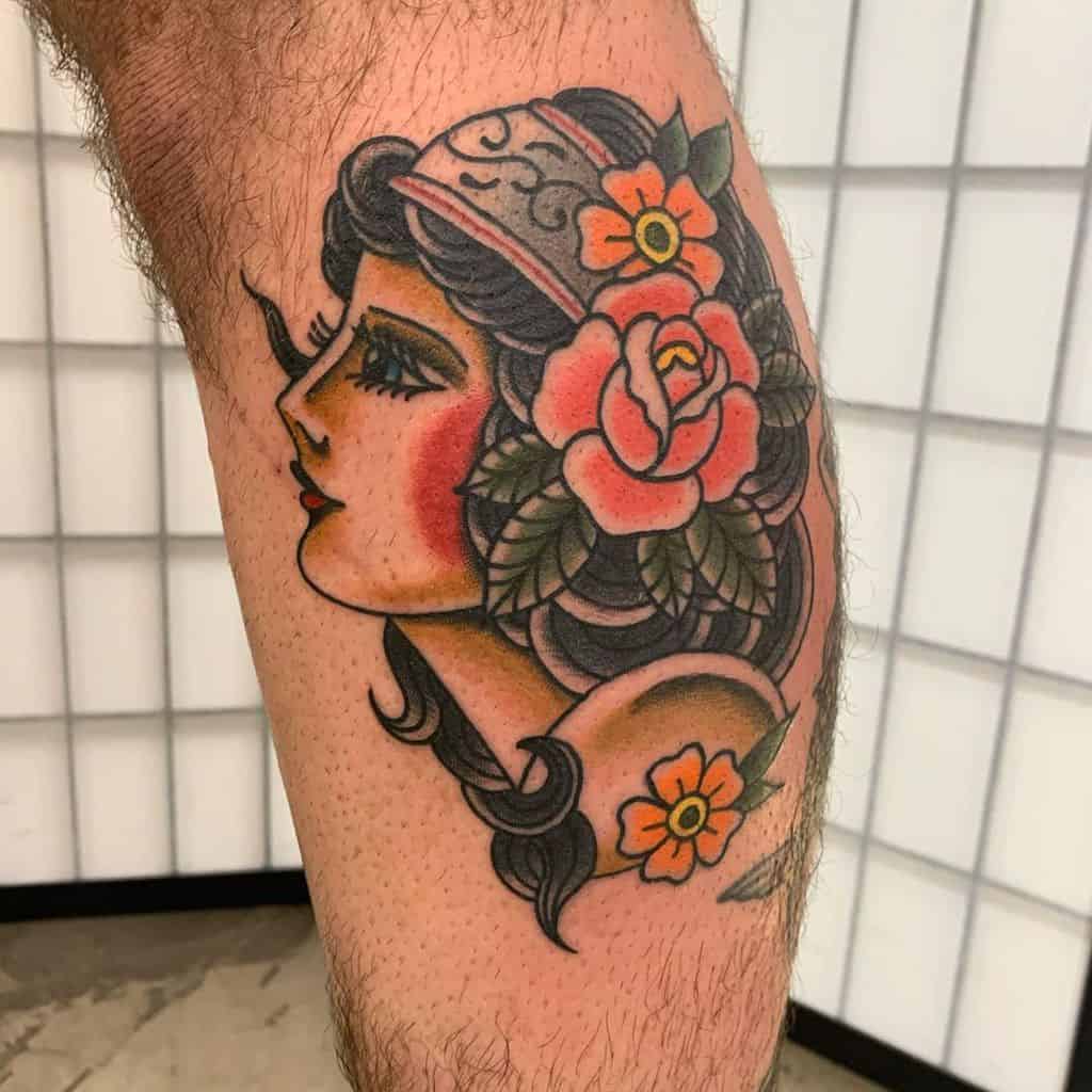 Traditional tattoo of a gypsy woman in profile with bold black hair, floral accents, and vintage shading on the leg.