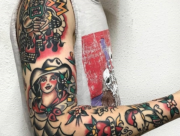Traditional American tattoo sleeve featuring bold black outlines, vibrant colors, and classic imagery like a cowgirl, dagger, and floral designs.
