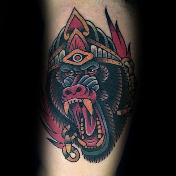 Neo-traditional baboon tattoo with bold colors, fierce expression, and tribal-inspired headdress, featuring a third eye for a mystical and powerful design.