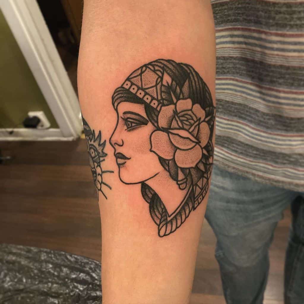 Bold blackwork tattoo of a gypsy woman with a headscarf, large rose, and intricate details on the forearm.