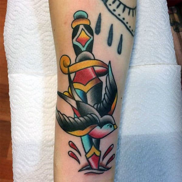 Tattoo of a dagger with a colorful handle and a bird in flight on the forearm
