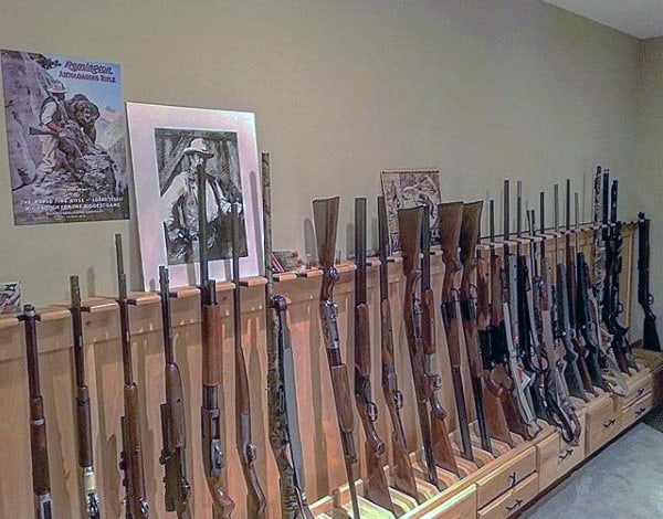 Gun room with wooden floor racks displaying rifles and vintage posters on the wall.