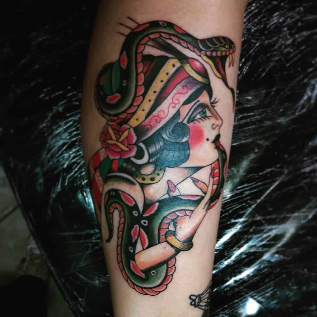 Traditional tattoo of a gypsy woman with a colorful headscarf and a coiled snake wrapping around her, featuring bold shading on the forearm.