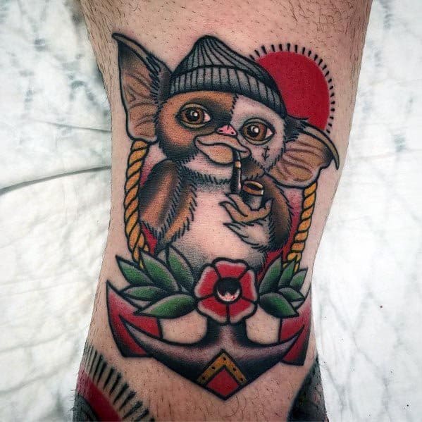 Traditional-style Gizmo tattoo with a sailor theme, featuring a beanie, pipe, anchor, and floral details for a unique nautical twist.