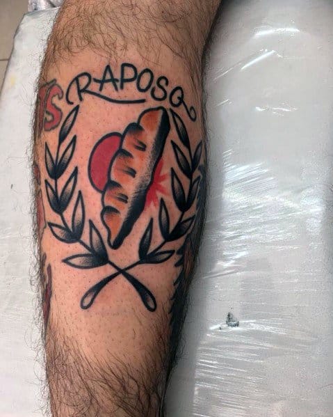 Colorful tattoo of a bread loaf with a red sunburst, crossed wheat branches, and the word "RAPOSO," creating a bold and traditional-style design.