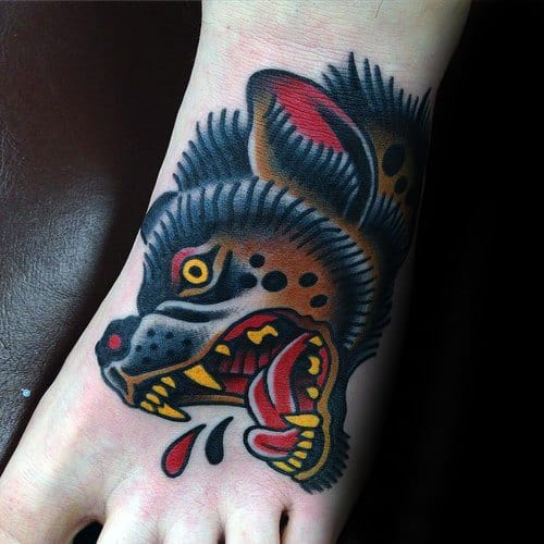 Traditional-style hyena tattoo on the foot with bold black outlines, vivid red and yellow accents, and a fierce snarling expression.