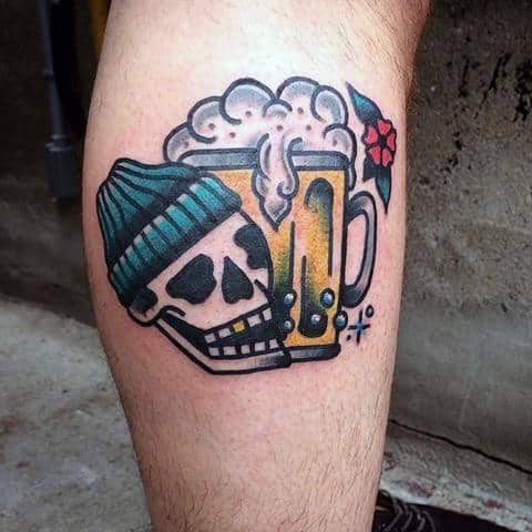 Traditional-style tattoo of a grinning skull in a beanie leaning against a frothy beer mug, with bold outlines, bright colors, and a small red flower accent.