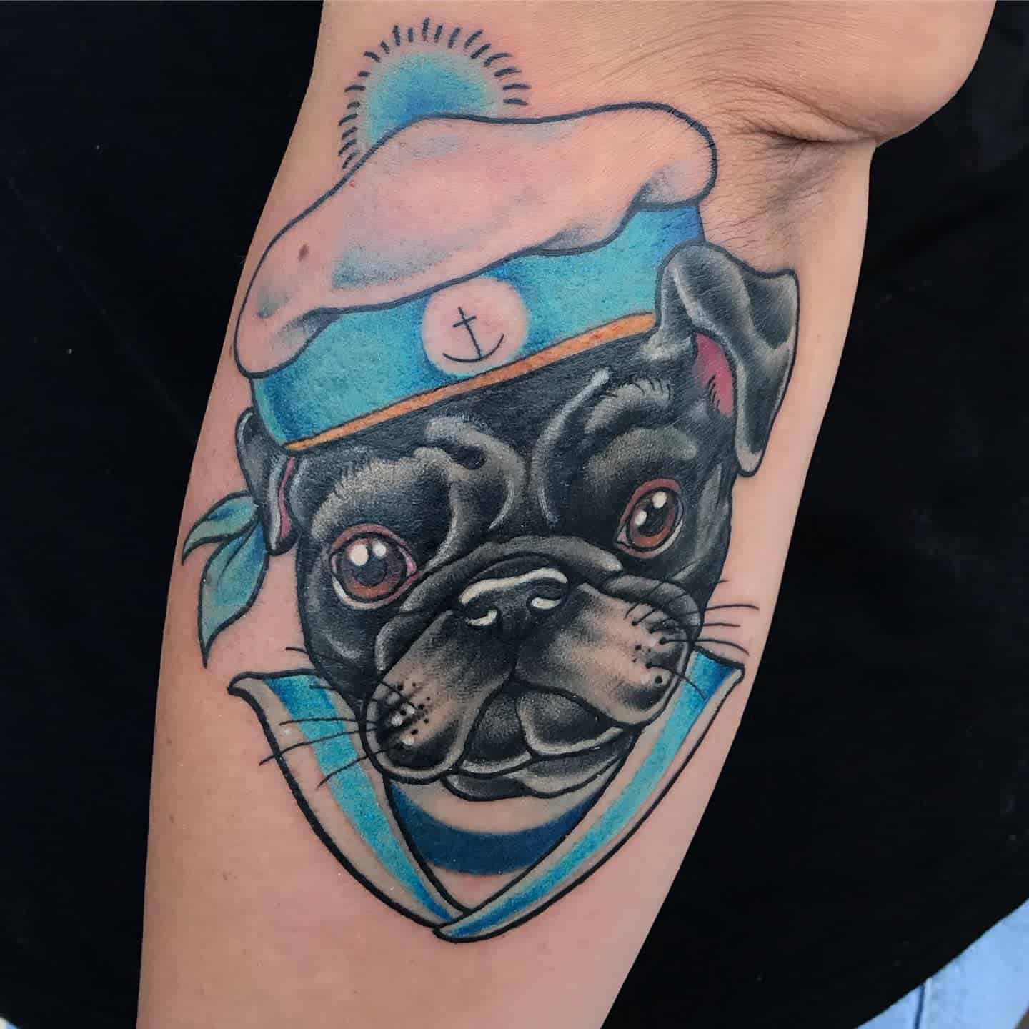 Tattoo of a pug in a sailor outfit with a blue and white hat, featuring an anchor emblem