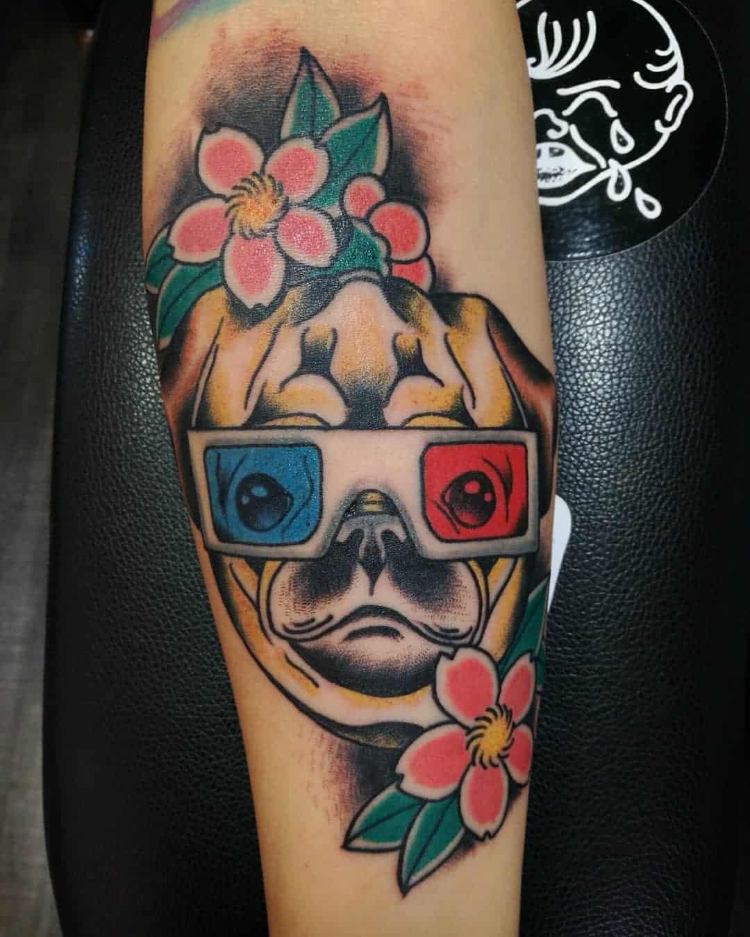 Tattoo of a pug wearing 3D glasses with red and blue lenses, surrounded by pink flowers