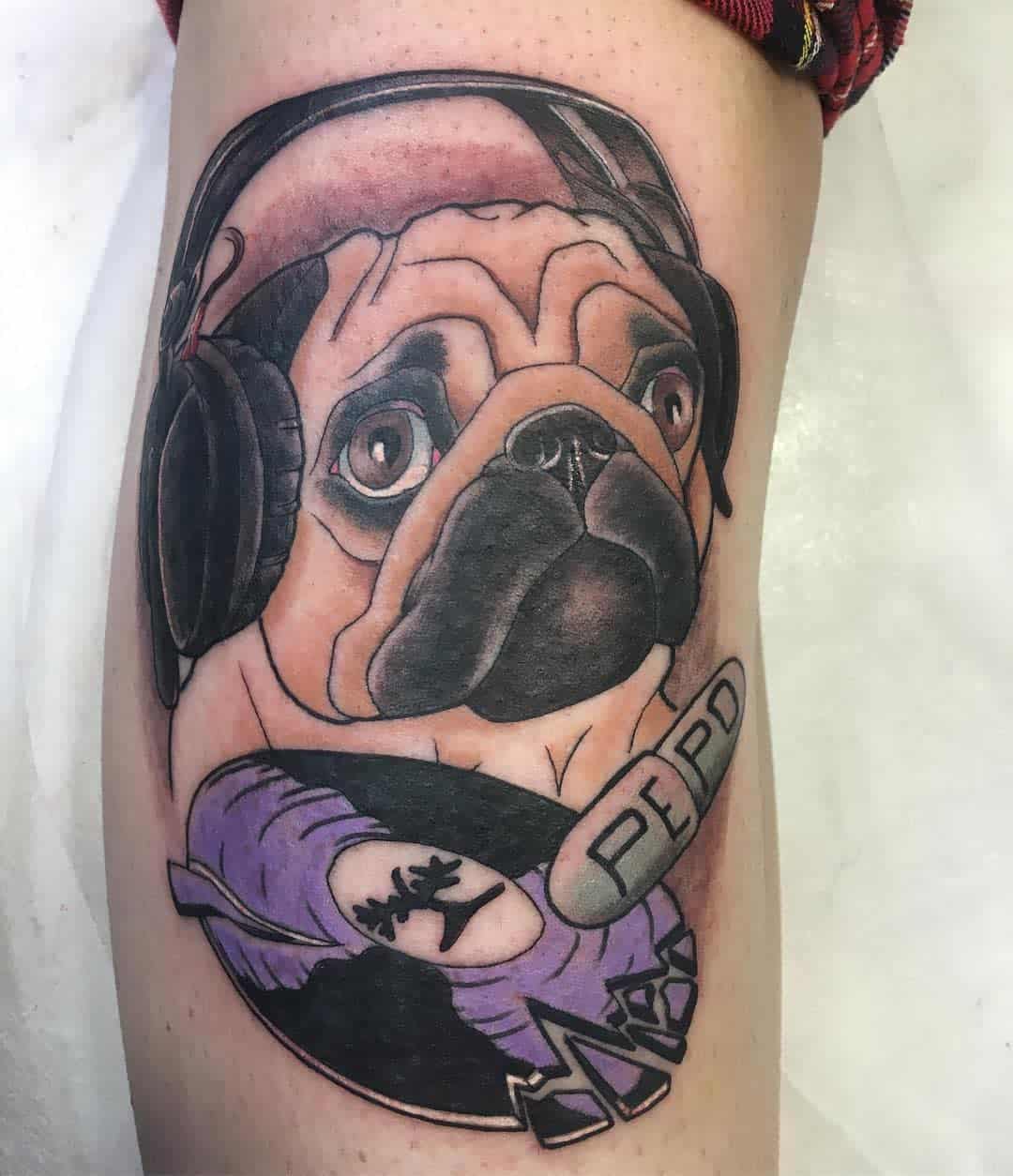 Tattoo of a pug wearing headphones and a bone labeled "PEPO," with a broken vinyl record underneath with tree in the center