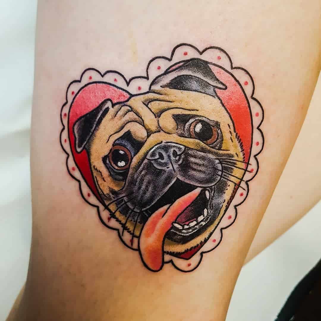 Tattoo of a pug with a wide smile, tongue out, set against a red heart background with a scalloped border