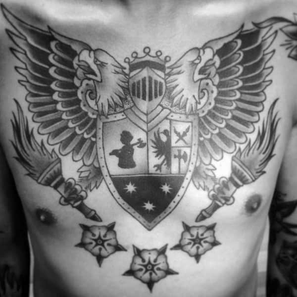 Symmetrical chest tattoo of a heraldic shield with four symbolic quadrants, flanked by eagle wings, torches, and floral emblems in black ink.