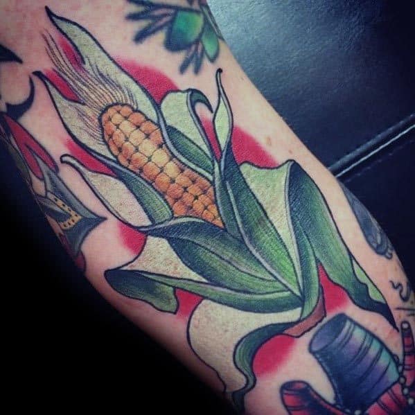 Bold tattoo of a corn cob with vibrant green husks and golden kernels, accented by a red background for a classic traditional style.