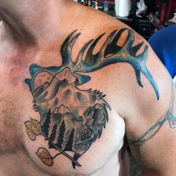 Colorful elk tattoo on the chest and shoulder, featuring a mountain landscape within the design, bold shading, and vibrant blue antlers.