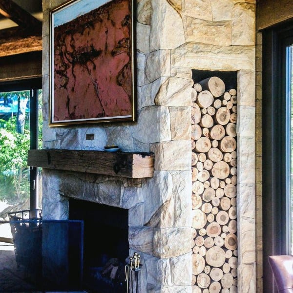 Rustic stone fireplace with a built-in log storage nook, a reclaimed wooden mantel, and a striking abstract painting above.