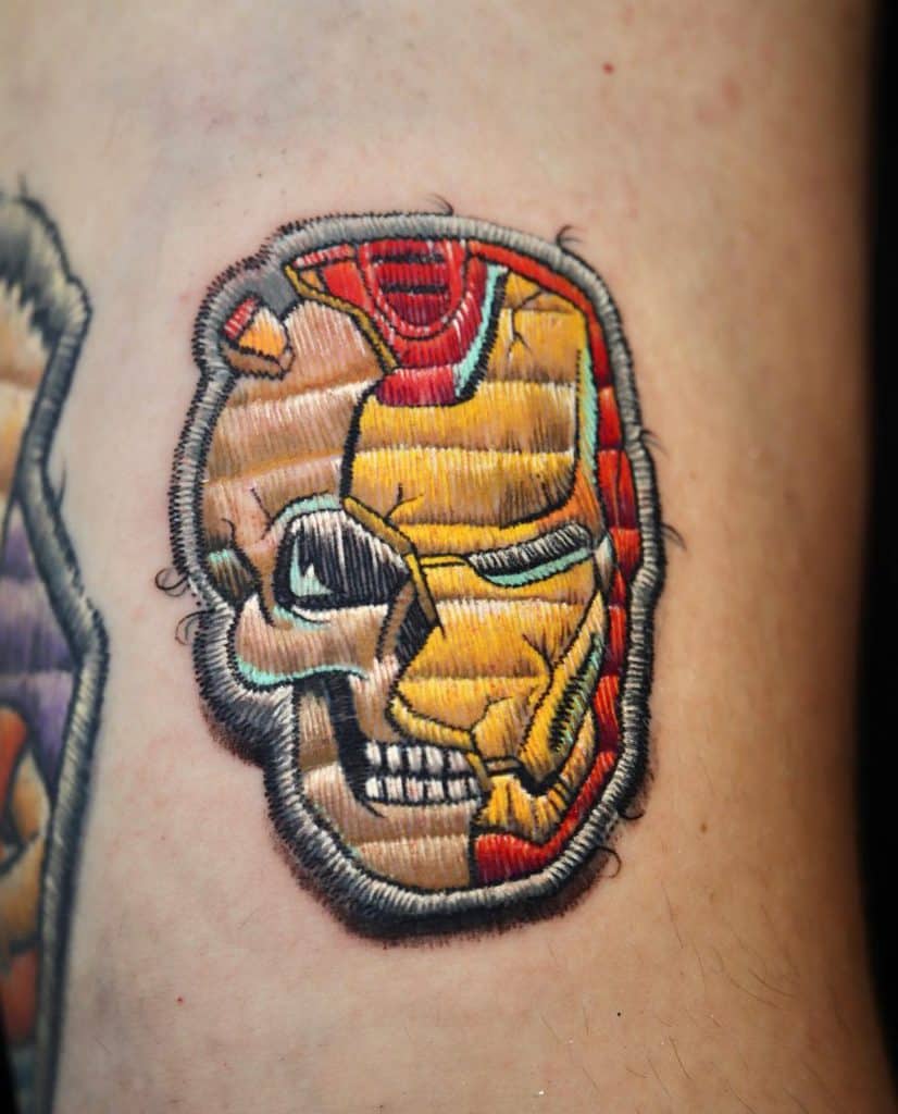 Realistic embroidered tattoo blending Iron Man's mask with a skull, designed with stitched details for a fabric illusion.