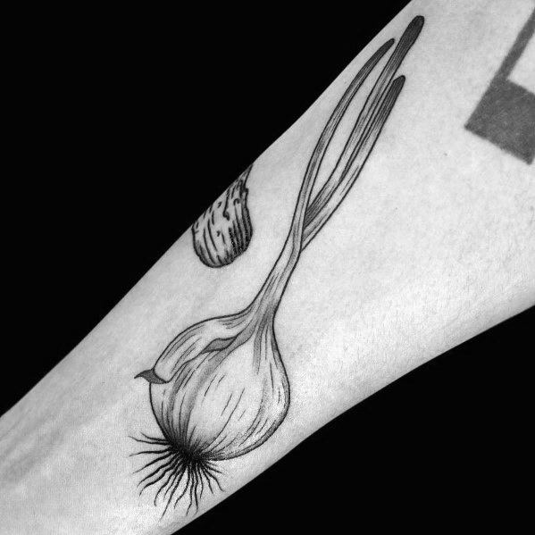Black and grey forearm tattoo of a detailed onion with long sprouting leaves and fine line shading, creating a realistic botanical design.