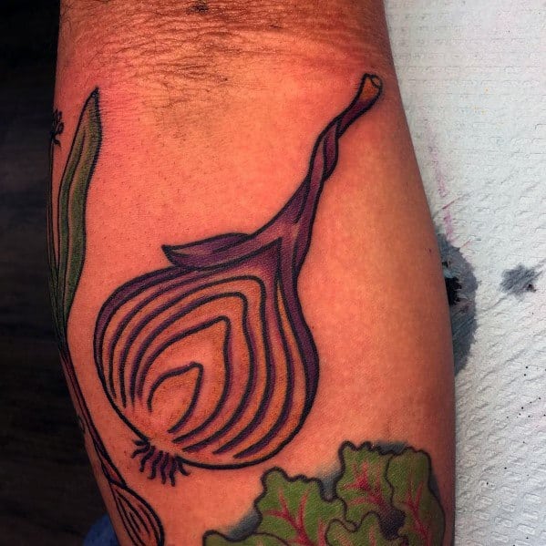 Bold and colorful tattoo of a sliced red onion with thick black outlines, vibrant shading, and leafy greens, blending traditional and modern styles.