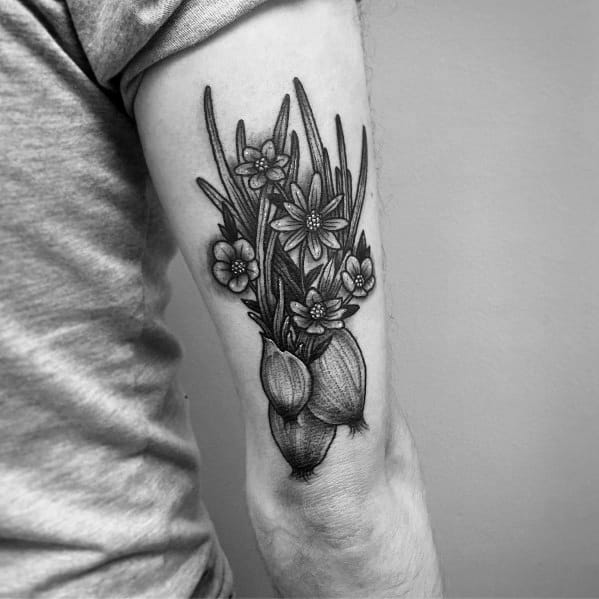 Black and grey tattoo of onions with blooming flowers and long leaves on the arm, featuring fine line details and intricate shading for a botanical look.