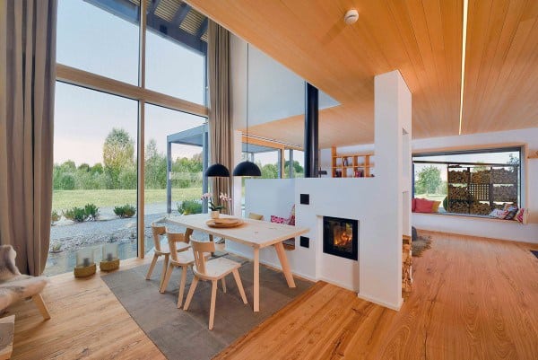 Modern living room with wooden floors, dining nook, fireplace, large windows, and a view of a garden