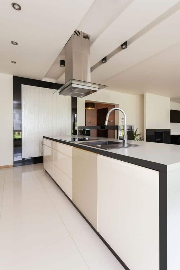 Minimalist kitchen with a white island, black countertop, stainless steel hood, and sleek design.
