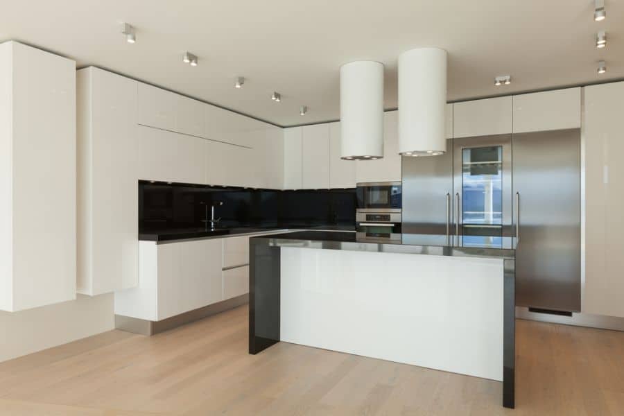 Modern kitchen with glossy white cabinets, black countertops, stainless steel appliances, and island.