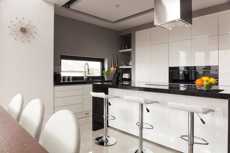 Modern kitchen with glossy white cabinets, black countertops, bar stools, and stainless steel hood.
