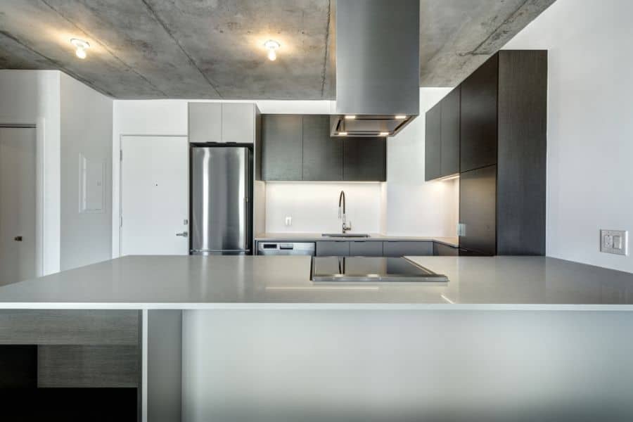 Modern kitchen with black cabinets, white countertops, stainless steel appliances, and concrete ceiling.