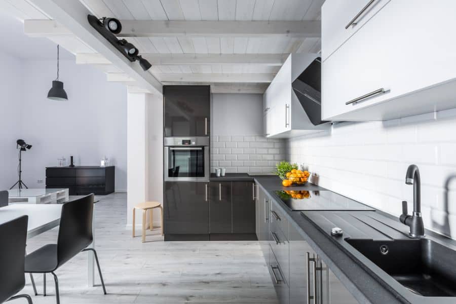 Modern kitchen with black countertops, white cabinets, subway tile backsplash, and exposed beams.