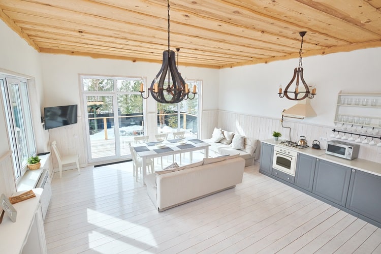 Bright airy kitchen with a wooden ceiling, white decor, modern lighting, and large windows overlooking the deck