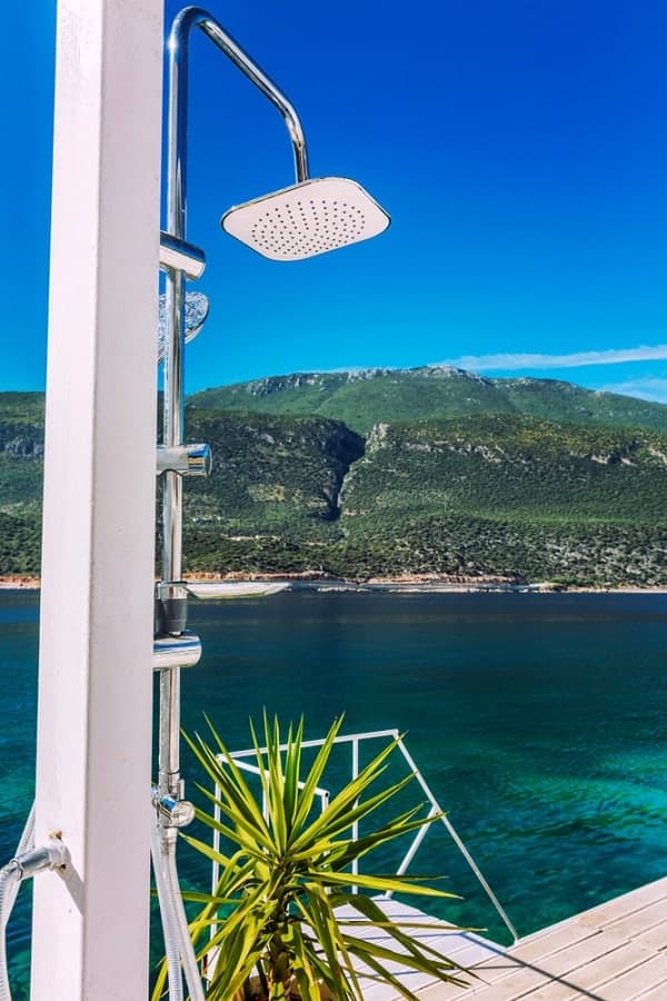 Outdoor shower with a sleek design overlooking a turquoise sea and lush green mountains.
