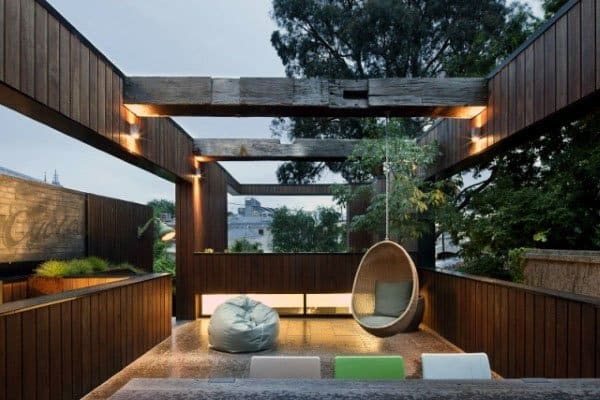 Contemporary open-roof pavilion with sleek wooden walls, modern seating, and a hanging chair for relaxation.
