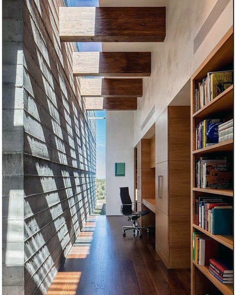 Modern home office with skylight ceiling, wood floors, and built-in bookshelves.