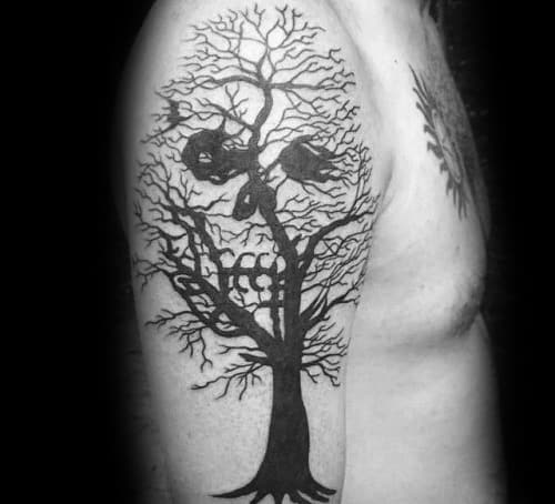 Silhouette tree tattoo with two hanging figures and hidden skull imagery formed by twisting branches on the upper arm.