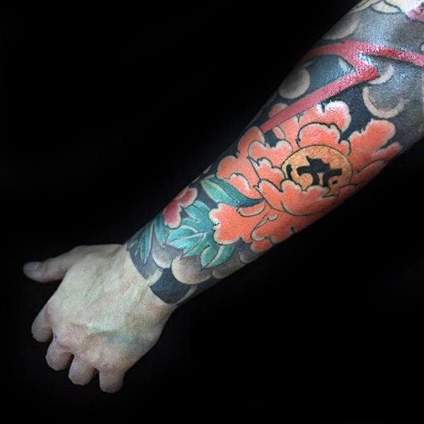 A vibrant Japanese-style forearm tattoo featuring bold orange flowers with green leaves and intricate cloud-like shading, giving the piece a rich, traditional aesthetic