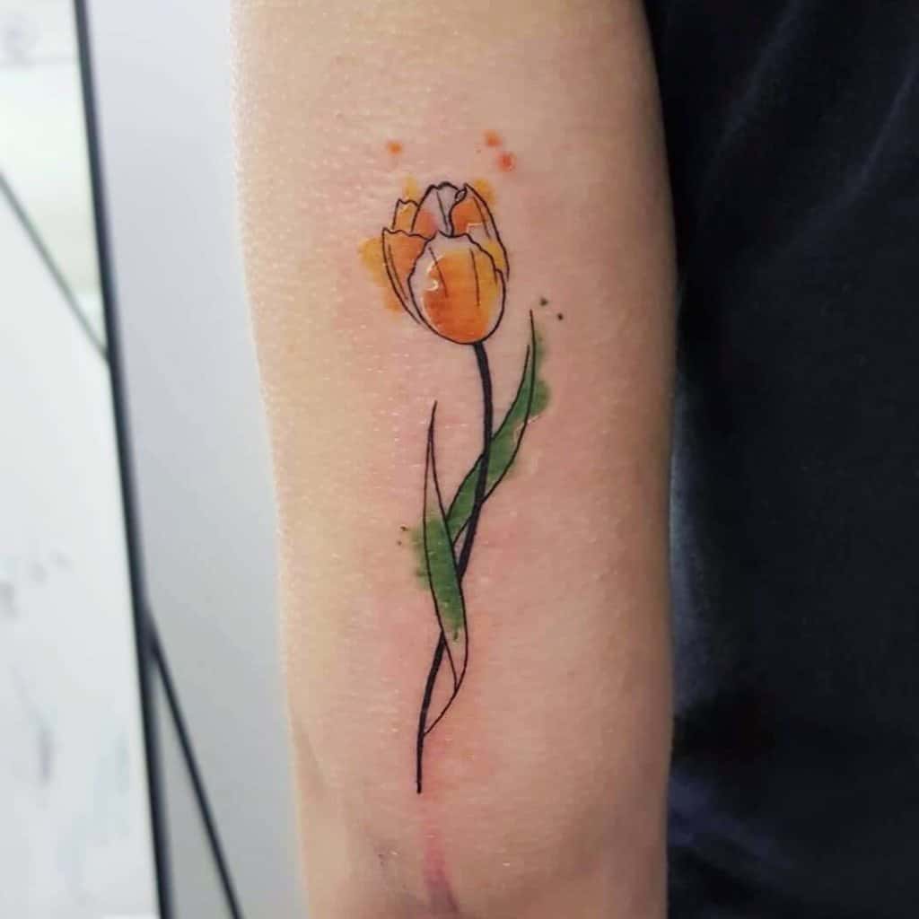 A watercolor-style tulip tattoo on the forearm, featuring an orange flower with green leaves and artistic ink splashes for a vibrant look.