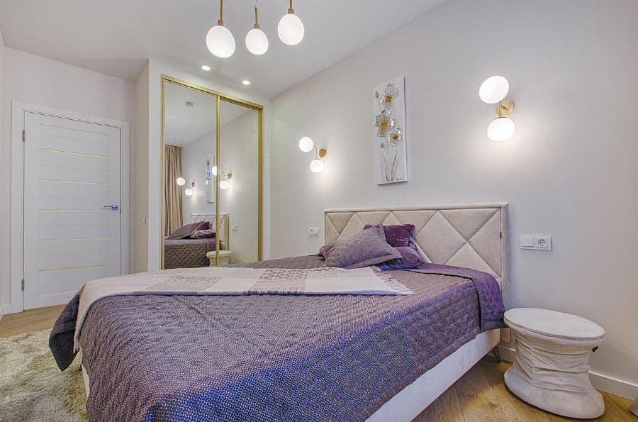 Bedroom with lavender bedding, tufted headboard, and orb ceiling and wall lights.