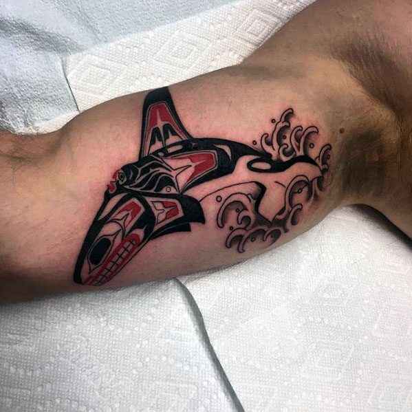 Bold black and red orca tattoo on the forearm, designed with tribal-inspired patterns and accompanied by stylized water splashes for dynamic effect.