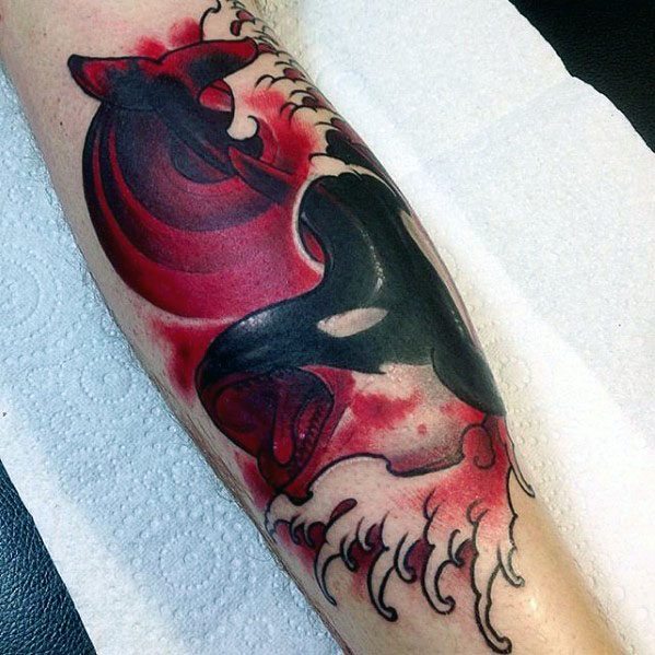 Bold black and red tattoo on the forearm, featuring an orca whale with dynamic, flowing waves and splashes, capturing a sense of power and movement with striking contrast.