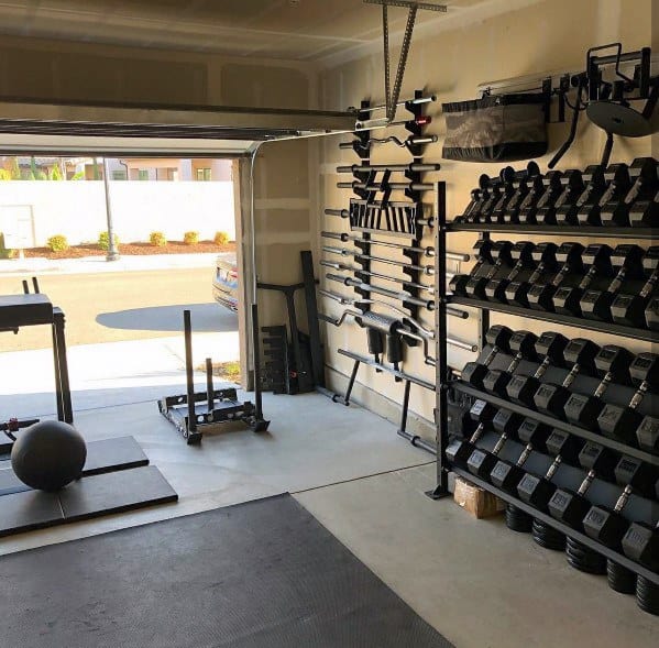 Organized garage gym with barbells, dumbbells, sled, and medicine ball storage.