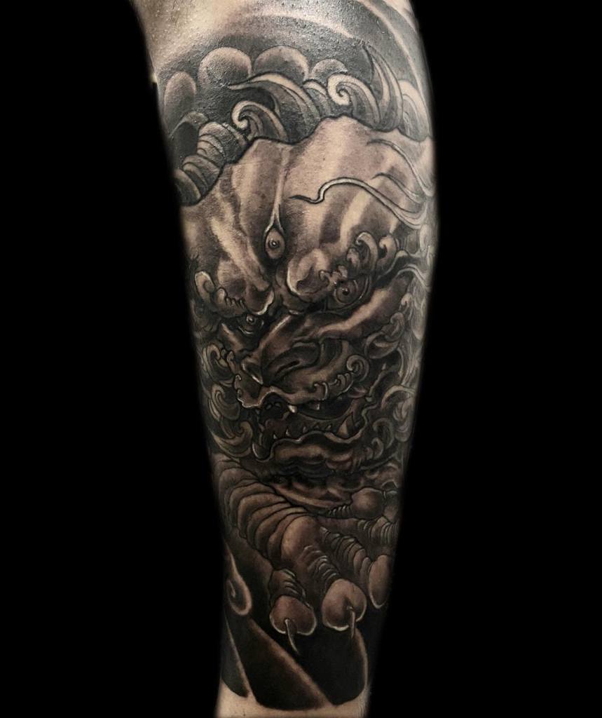 A detailed black and gray leg sleeve tattoo of a dragon, featuring swirling clouds and intricate scales