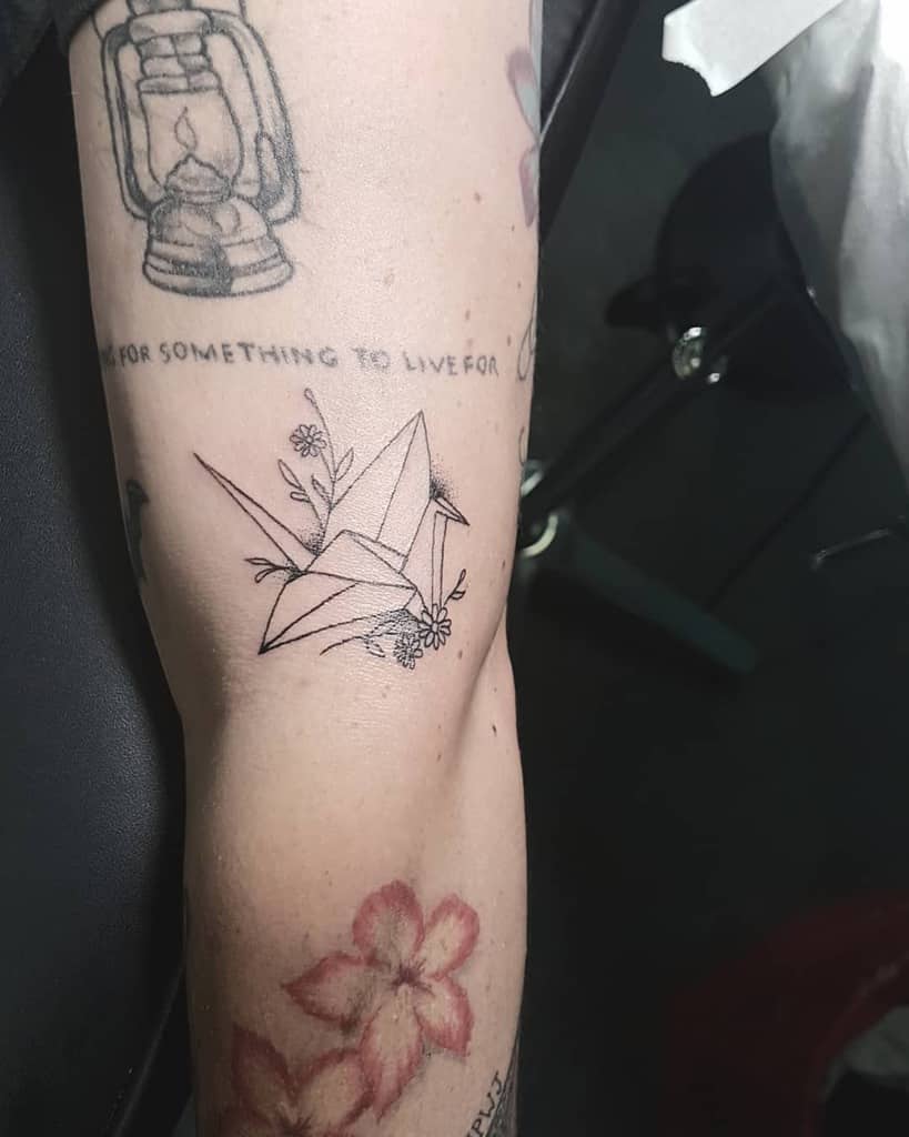 Bicep tattoo black and grey fine line origami bird daisy