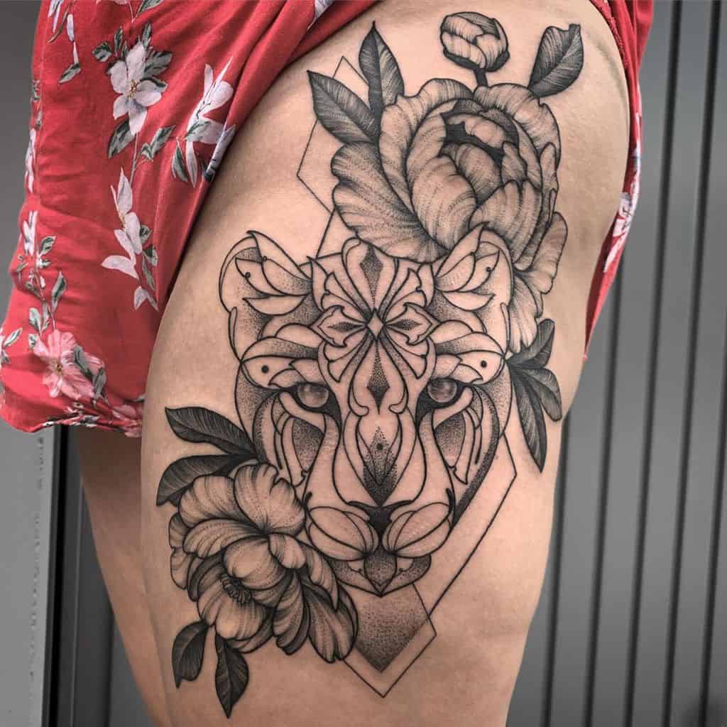 Bold black and grey lioness thigh tattoo with geometric patterns, intricate floral details, and dotwork shading for a striking design.