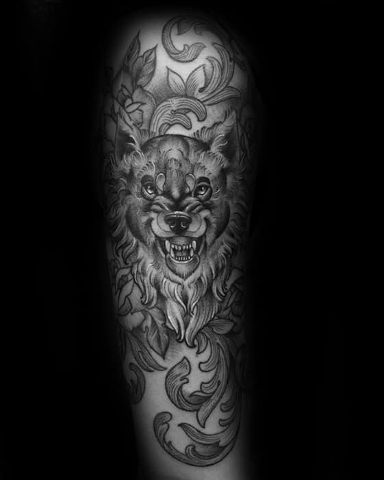 Tattoo of a snarling wolf surrounded by intricate floral designs on a person's arm