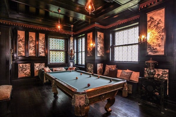 Ornate billiard room with dark wood paneling, decorative windows, and vintage lighting fixtures.